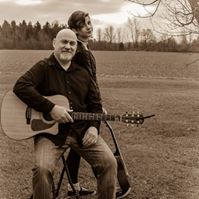 Man on stool with guitar and younger man standing with guitar