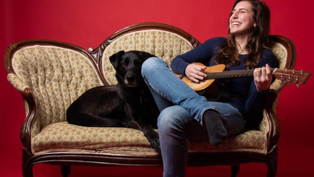 Woman playing guitar on couch with black dog