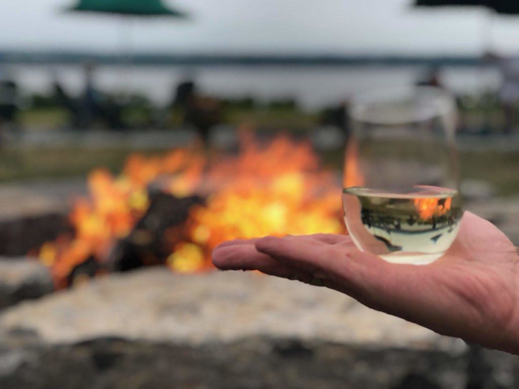 Hand balancing glass of white wine with fire in background