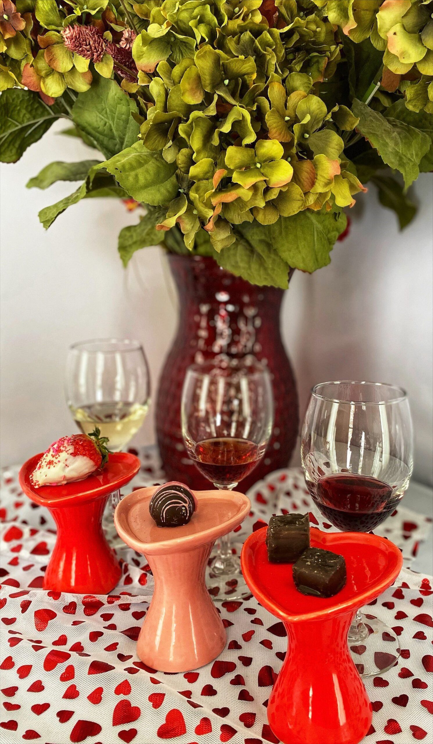 vase with flowers in the background, three chocolates and three glasses of wine in the foreground at Miles Wine Cellars