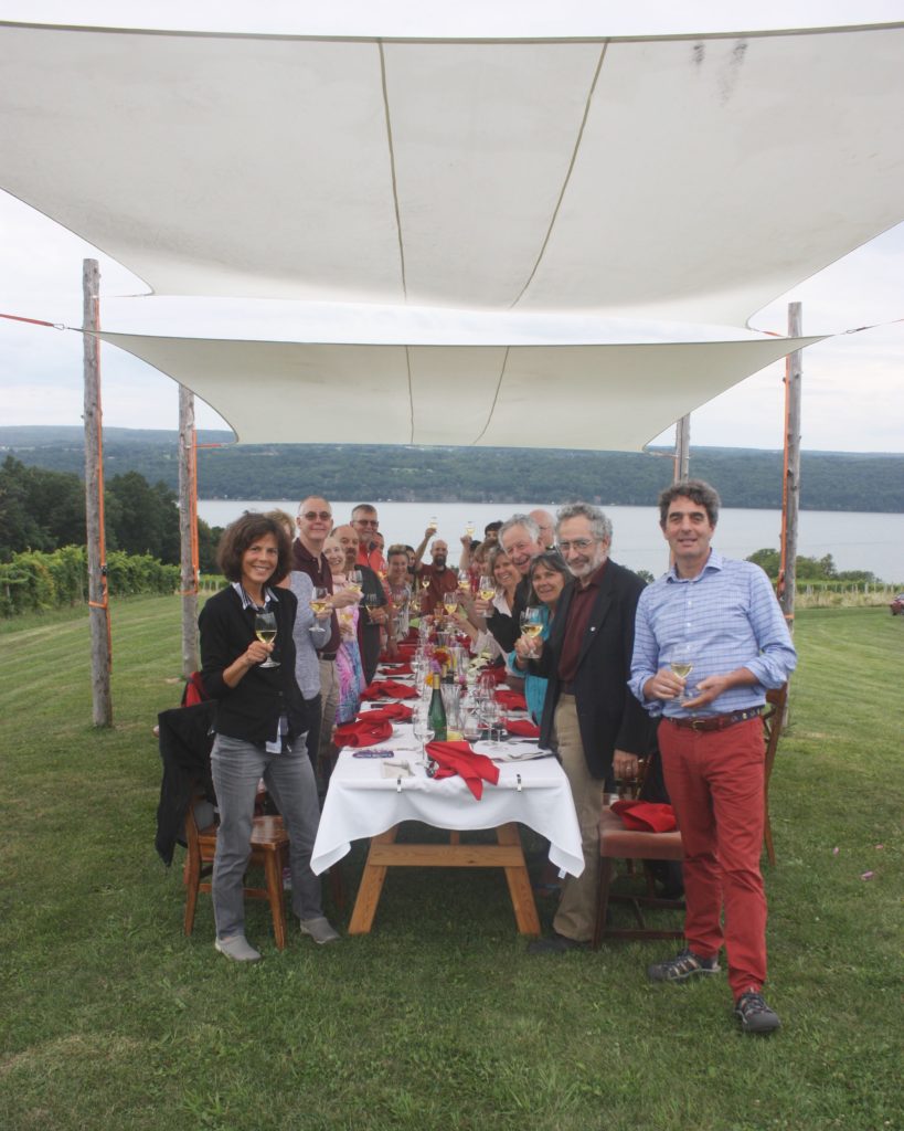 People standing around a table with canopy, overlooking Seneca Lake