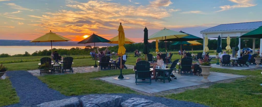 Sunset over Seneca Lake with picnic tables and umbrellas, people sitting outside