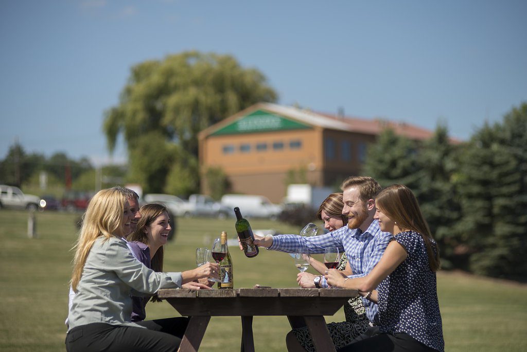 A group of friends enjoying a bottle of wine from Glenora Winery while sitting on at a picnic table on the property