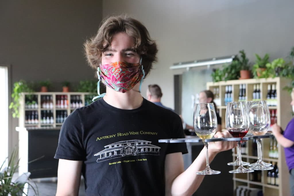 Server following COVID guidelines by wearing a mask while holding a wine flight